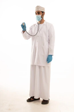 اتباع اجراءات السلامة للوقاية من فايروس كورونا،  بورتريه لطبيب عربي خليجي عماني يرتدي الدشداشة والعمامة والمعطف الطبي و الكمامة يضع السماعة الطبية يعمل في القطاع الصحي، الجسم بالطول الكامل، خلفية بيضاء