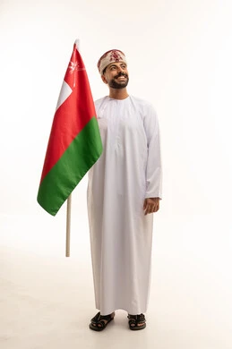 رجل عماني بالزي التقليدي يحمل علم سلطنة عمان