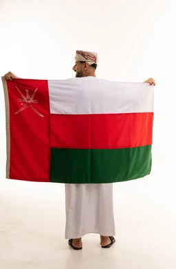 رجل عماني يحمل العلم الوطني بالزي التقليدي