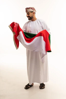 رجل عماني بالزي التقليدي يحمل علم سلطنة عمان