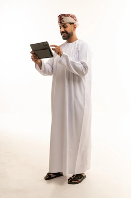 رجل عماني بالدشداشة التقليدية يستخدم جهاز لوحي