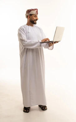 رجل عماني يستخدم الكمبيوتر المحمول بالدشداشة التقليدية