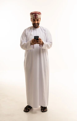 رجل عماني يستخدم الهاتف الذكي بالزي التقليدي الأبيض