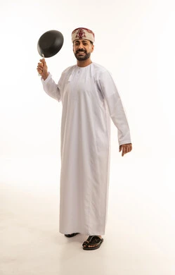 رجل عماني بالزي التقليدي يمسك مقلاة طبخ