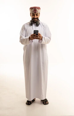 رجل عُماني بالزي التقليدي يستخدم الهاتف الذكي
