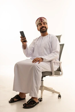 رجل عُماني يحمل هاتف ذكي على كرسي مكتب