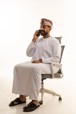 رجل عُماني بزي تقليدي يتحدث بالهاتف على كرسي مكتب