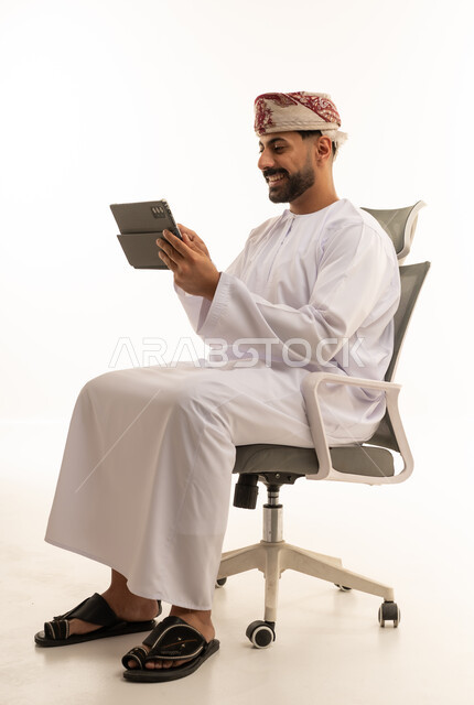 رجل عماني يستخدم جهاز لوحي على كرسي مكتب