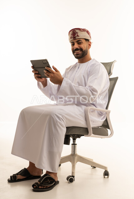 رجل عُماني مع جهاز لوحي يجلس على كرسي مكتب