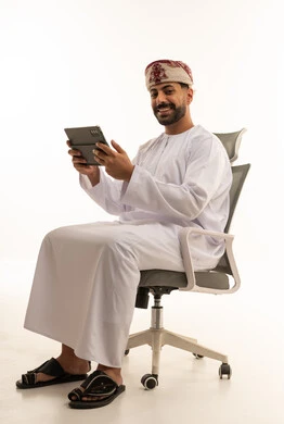 رجل عُماني مع جهاز لوحي يجلس على كرسي مكتب