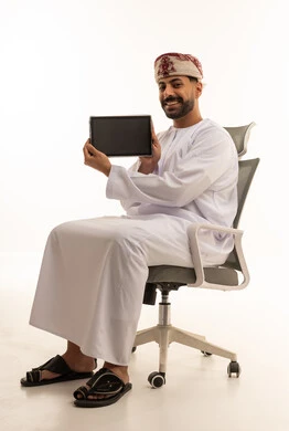 رجل عماني يحمل جهاز لوحي ويجلس على كرسي مكتب
