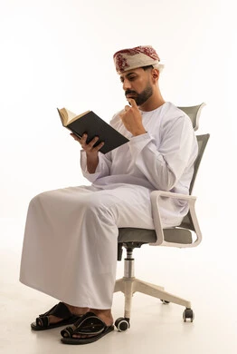 رجل عُماني بالزي التقليدي يقرأ كتاباً في الاستوديو