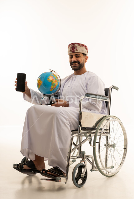 رجل عماني على كرسي متحرك يحمل مجسم الكرة الأرضية