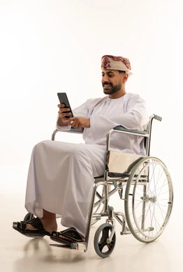رجل عُماني على كرسي متحرك يستخدم هاتف ذكي خلفية بيضاء