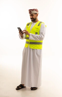 رجل عماني بسترة سلامة يستخدم الهاتف الذكي