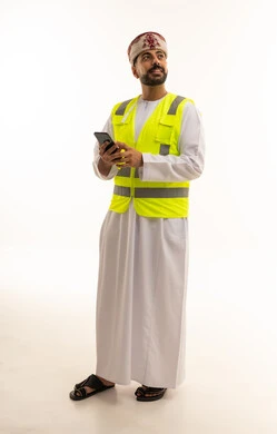 مهندس عماني يرتدي سترة السلامة ويمسك هاتف ذكي
