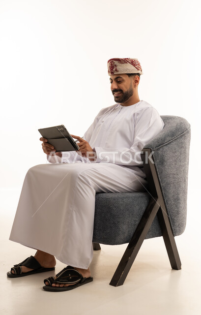 رجل عُماني بالزي التقليدي يستخدم جهازاً لوحياً في الاستوديو