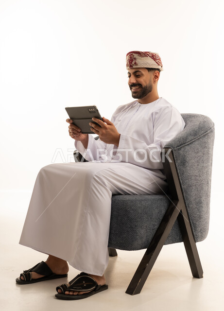 رجل عماني بالزي التقليدي يستخدم جهاز لوحي ذكي في الاستوديو