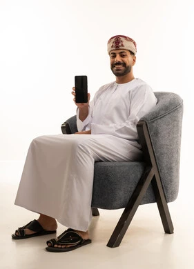 رجل عُماني يحمل هاتفاً ذكياً جالساً على كرسي