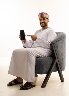 رجل عُماني يشير إلى هاتفه الذكي بالزي التقليدي