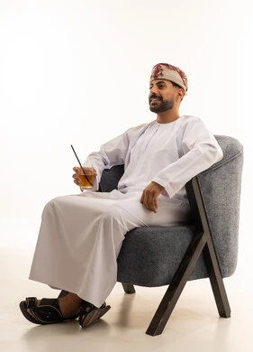 رجل عماني بالزي التقليدي يجلس على كرسي عصري