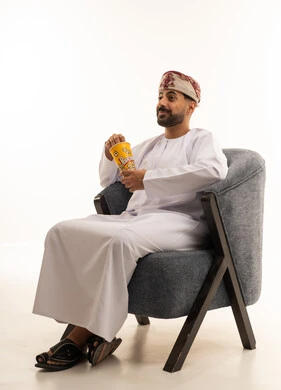 رجل عُماني يرتدي الزي التقليدي يجلس ويمسك علبة فشار