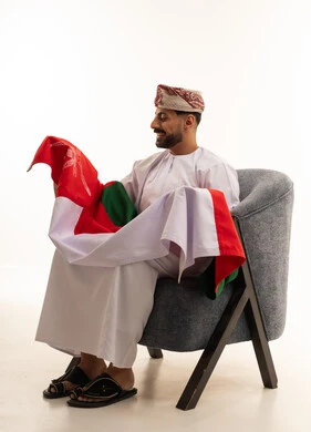 رجل عماني بالزي التقليدي يمسك علم سلطنة عمان