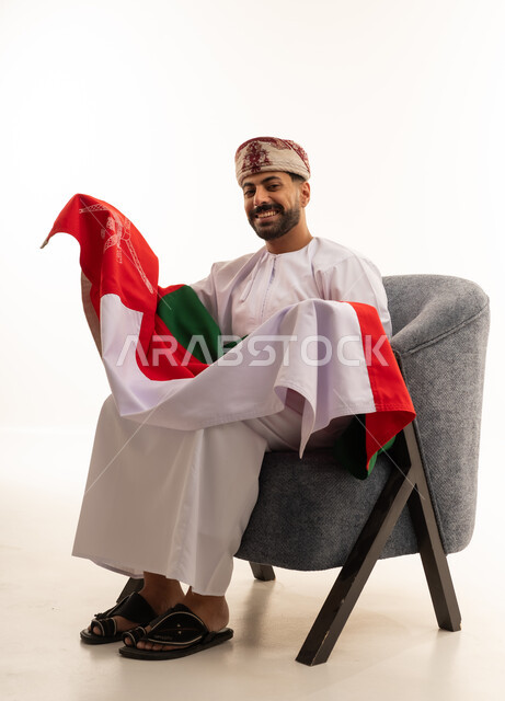رجل عُماني بالزي التقليدي يحمل علم سلطنة عُمان