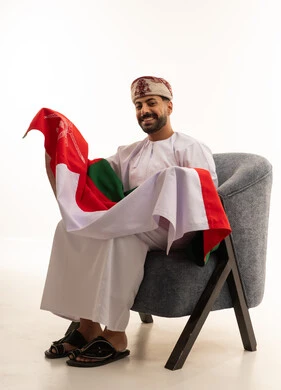 رجل عُماني بالزي التقليدي يحمل علم سلطنة عُمان