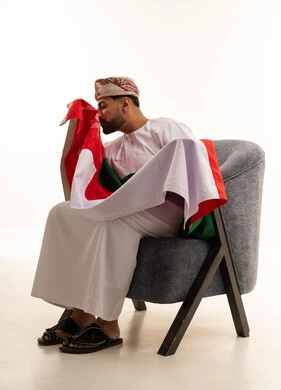 رجل عماني بالزي التقليدي يقبل علم سلطنة عمان