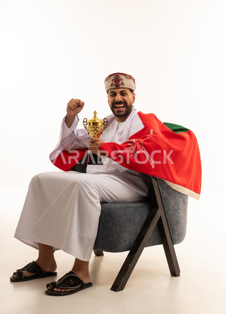 رجل عماني يحمل كأس ذهبي وعلم عمان