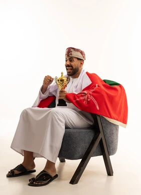 رجل عُماني يحمل كأساً ذهبياً وعلم عُمان يحتفل بالنجاح