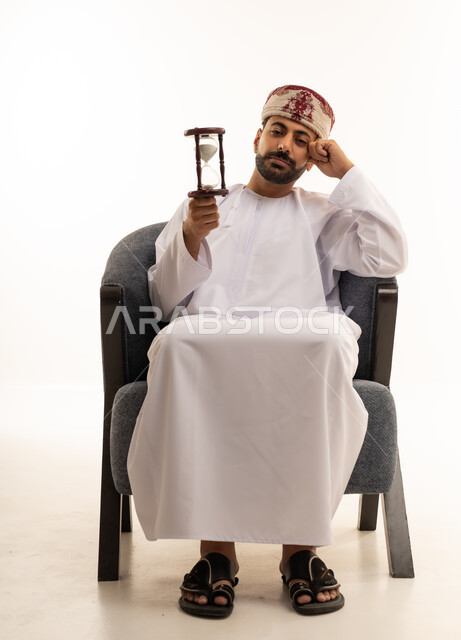 رجل عماني يحمل ساعة رملية بخلفية بيضاء