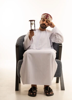رجل عماني يحمل ساعة رملية بخلفية بيضاء