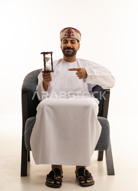 رجل عماني بالزي التقليدي يمسك ساعة رملية