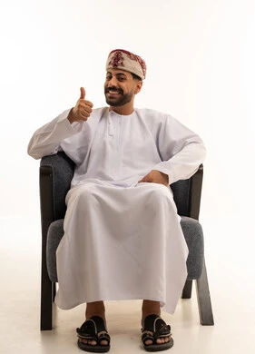 رجل عُماني يرتدي الدشداشة والكمة التقليدية ويشير بالإبهام
