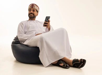 رجل عُماني مع هاتف ذكي على مقعد محشو