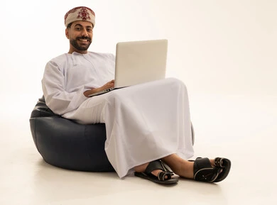رجل عُماني بالزي التقليدي يستخدم لابتوب في الاستوديو