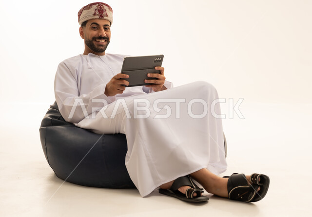 رجل عماني بجهاز لوحي على مقعد مريح
