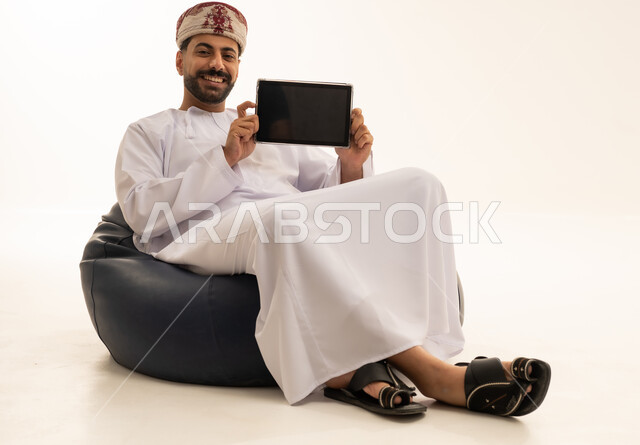 رجل عماني يمسك جهاز لوحي على خلفية بيضاء
