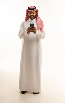 رجل سعودي بالثوب التقليدي يستخدم الهاتف الذكي بخلفية بيضاء