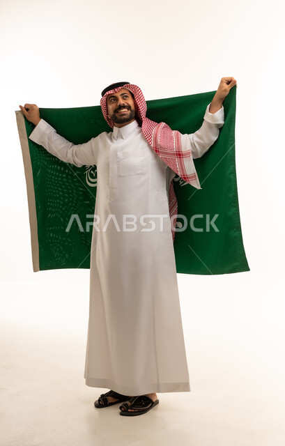 رجل سعودي بالزي التقليدي يحمل علم المملكة العربية السعودية