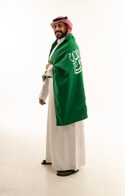 Saudi Man in Traditional Thobe Wrapping Saudi Flag