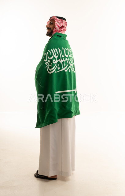 رجل سعودي يرتدي الزي التقليدي وملتف بالعلم الوطني