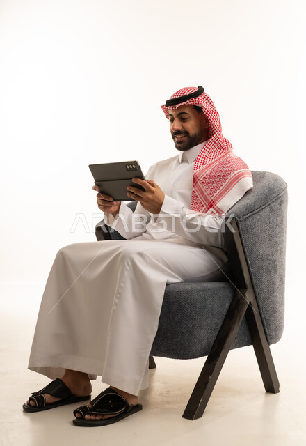رجل سعودي بالثوب التقليدي يستخدم جهاز لوحي