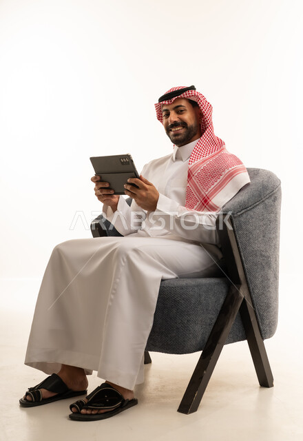 رجل سعودي بالثوب يستخدم جهاز لوحي على الكرسي