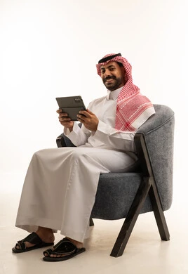 رجل سعودي بالثوب يستخدم جهاز لوحي على الكرسي