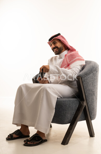 رجل سعودي بالزي التقليدي يجلس مع هاتف ذكي