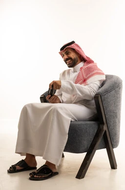 رجل سعودي بالزي التقليدي يجلس مع هاتف ذكي