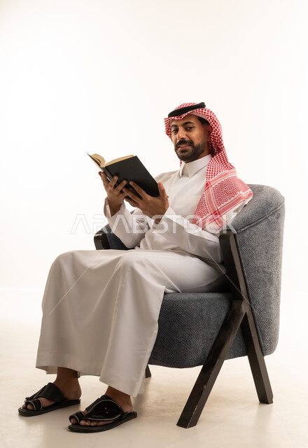 رجل سعودي بالثوب التقليدي يقرأ كتاباً